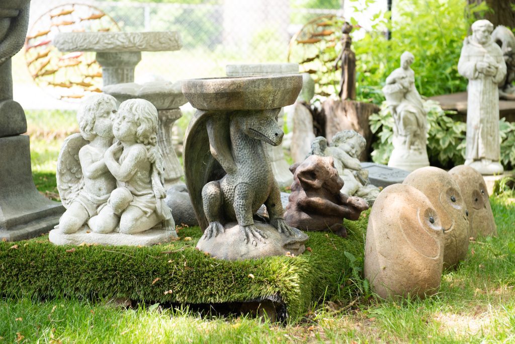 Several concrete garden sculptures arranged on a grassy area, with a dragon birdbath and two small angel statues prominent in the foreground.